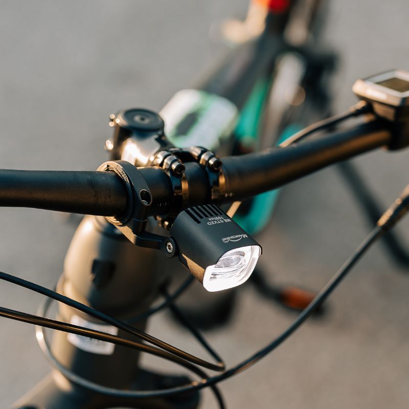 Magicshine ME StVZO 100LUX pod riadidlami elektrobicykla vedľa cyklopočítača za denného svetla