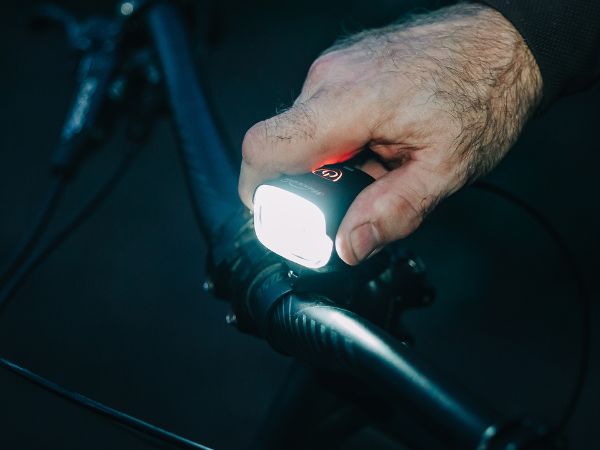 Cyklista potme drží rozsvietené Magicshine MJ-902S na riadidlách, na tlačidle svieti indikátor