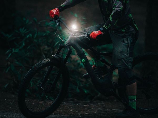 Jazdec s elektrobicyklom v nočnom lese, predné svetlo Magicshine MJ-906S svieti z riadidiel