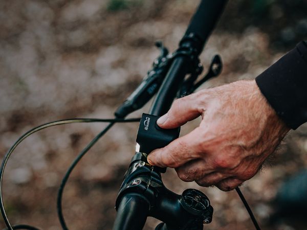 Ruka bez rukavice ovláda veľké tlačidlo na hornej strane svetla Magicshine MJ-906S na riadidlách bicykla