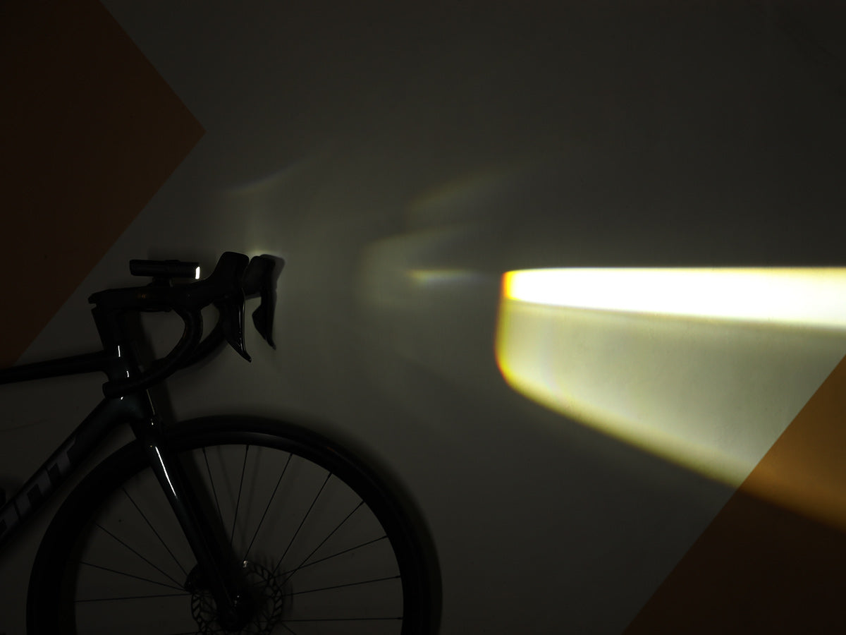 L&uacute;č Magicshine MK 150 StVZO premietnut&yacute; na stenu vedla cestn&eacute;ho bicykla s vodorovnou hranou