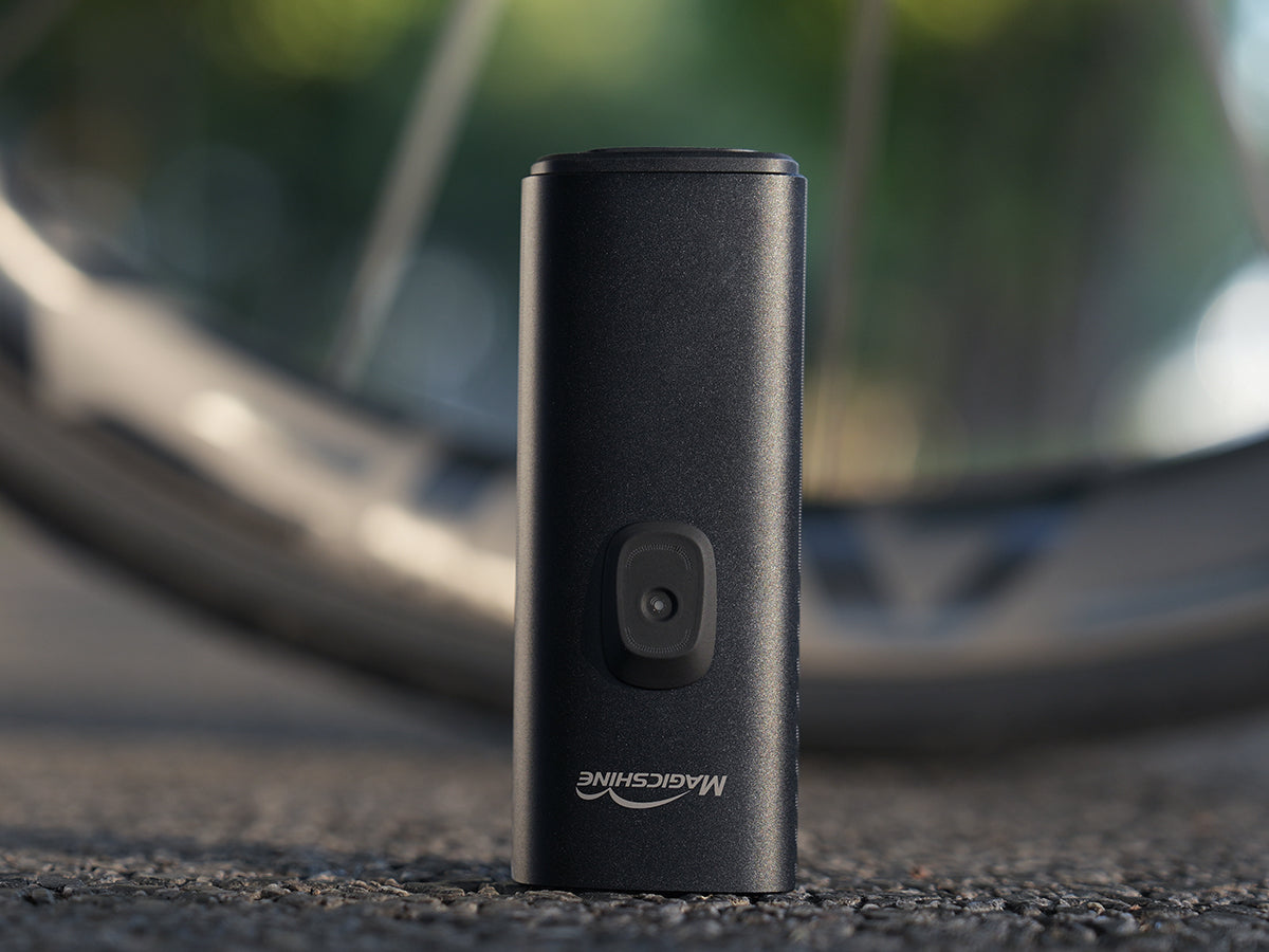 Magicshine MK 150 StVZO postaven&eacute; na asfalte, hlin&iacute;kov&eacute; telo s tlačidlom a logom Magicshine
