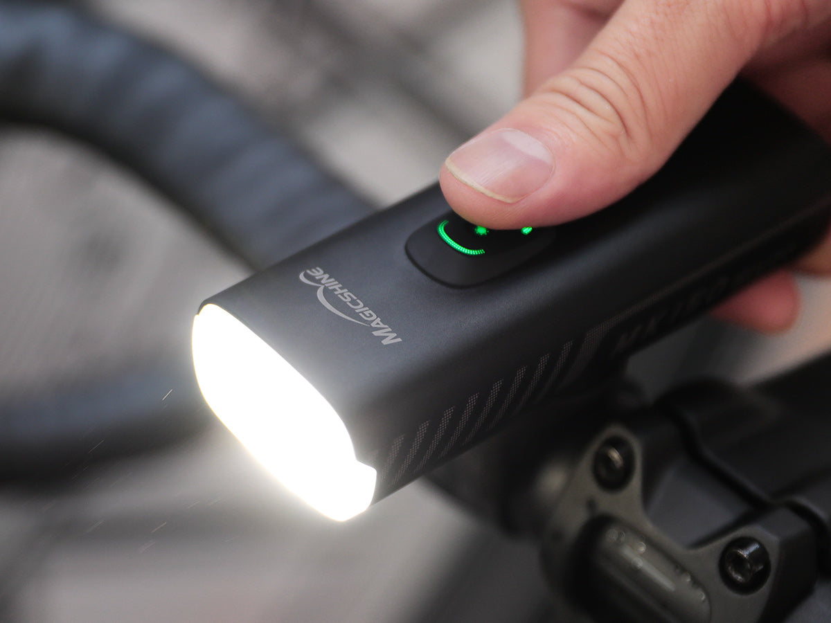 Palec na sp&iacute;nači Magicshine MK 150 StVZO, v tlačidle svieti dvojdieln&yacute; zelen&yacute; indik&aacute;tor v&yacute;konu