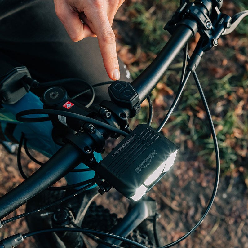 Ruka stláča bezdrôtový ovládač Magicshine MJ-6508 na predstavci, MONTEER 12000 je upnutý na riadidlách horského bicykla