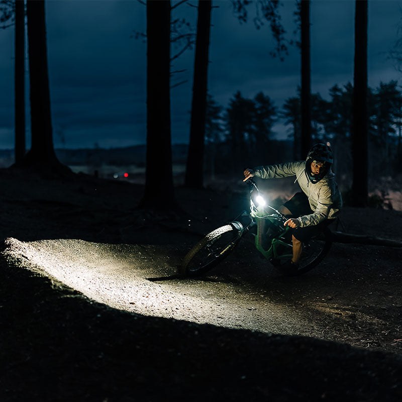 Magicshine MONTEER 12000 osvetľuje nočný lesný trail — jazdec na horskom bicykli v širokom svetelnom kuželi
