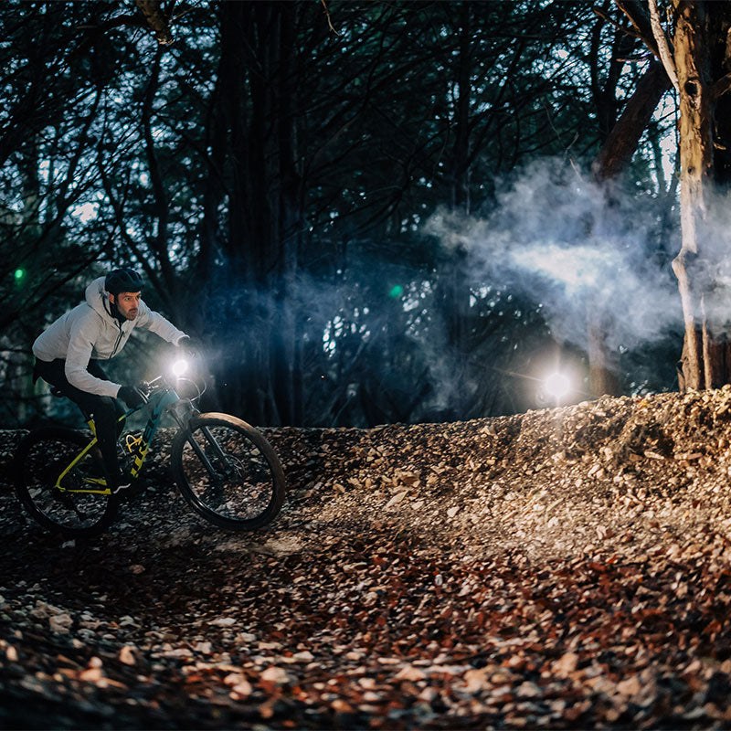Jazdec na horskom bicykli v nočnom lese, MONTEER 12000 preráža lúčom zvírený prach nad chodníkom