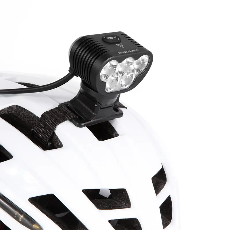 Magicshine MONTEER 5000S upevnené cez popruh na bielej cyklistickej prilbe, k svetlu vedie kábel k akumulátoru