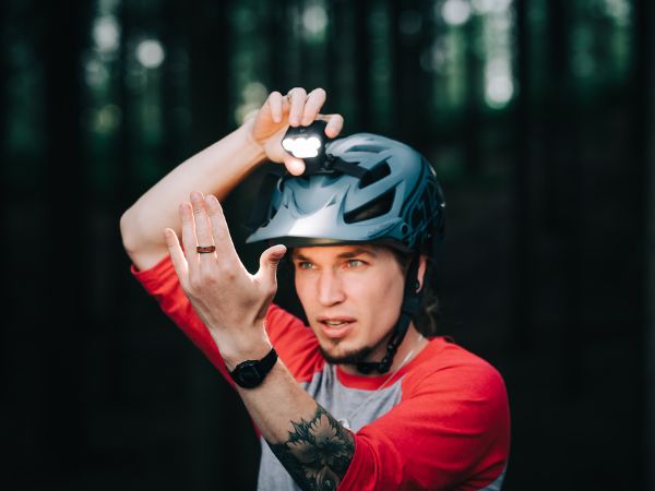 Cyklista si nasadzuje rozsvietené svetlo Magicshine Monteer 6500S V2.0 na prilbu pred nočnou jazdou v lese