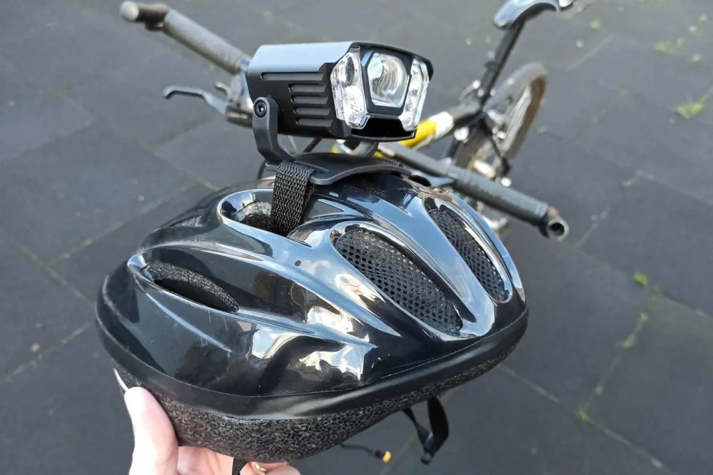 Cyklistická prilba so svietidlom Magicshine MONTEER 12000 v ruke, v pozadí bicykel pripravený na jazdu