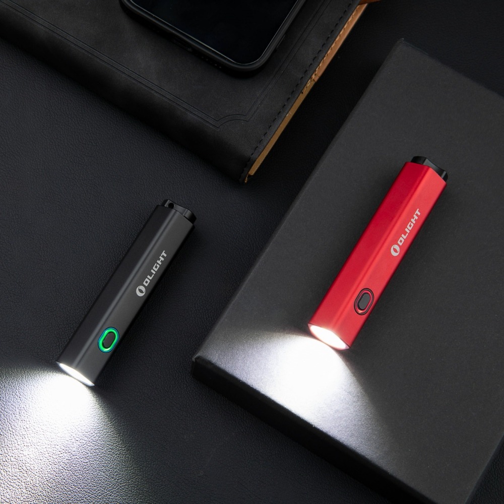 Olight Diffuse čierna so zeleným prstencom okolo spínača svieti na tmavom stole vedľa červenej Diffuse
