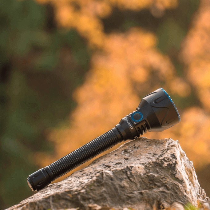 Olight Javelot Pro 2 leží na skale, hlava vpravo hore, modrý vrúbkovaný lem a hlboké vrúbkovanie po tele