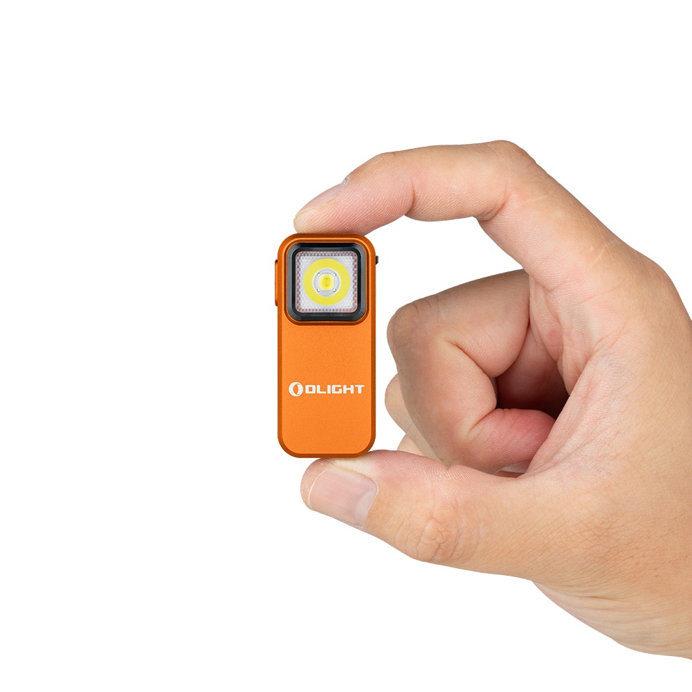Olight Oclip Orange medzi palcom a ukazovákom ukazuje veľkosť oranžového tela s čiernym lemom a LED