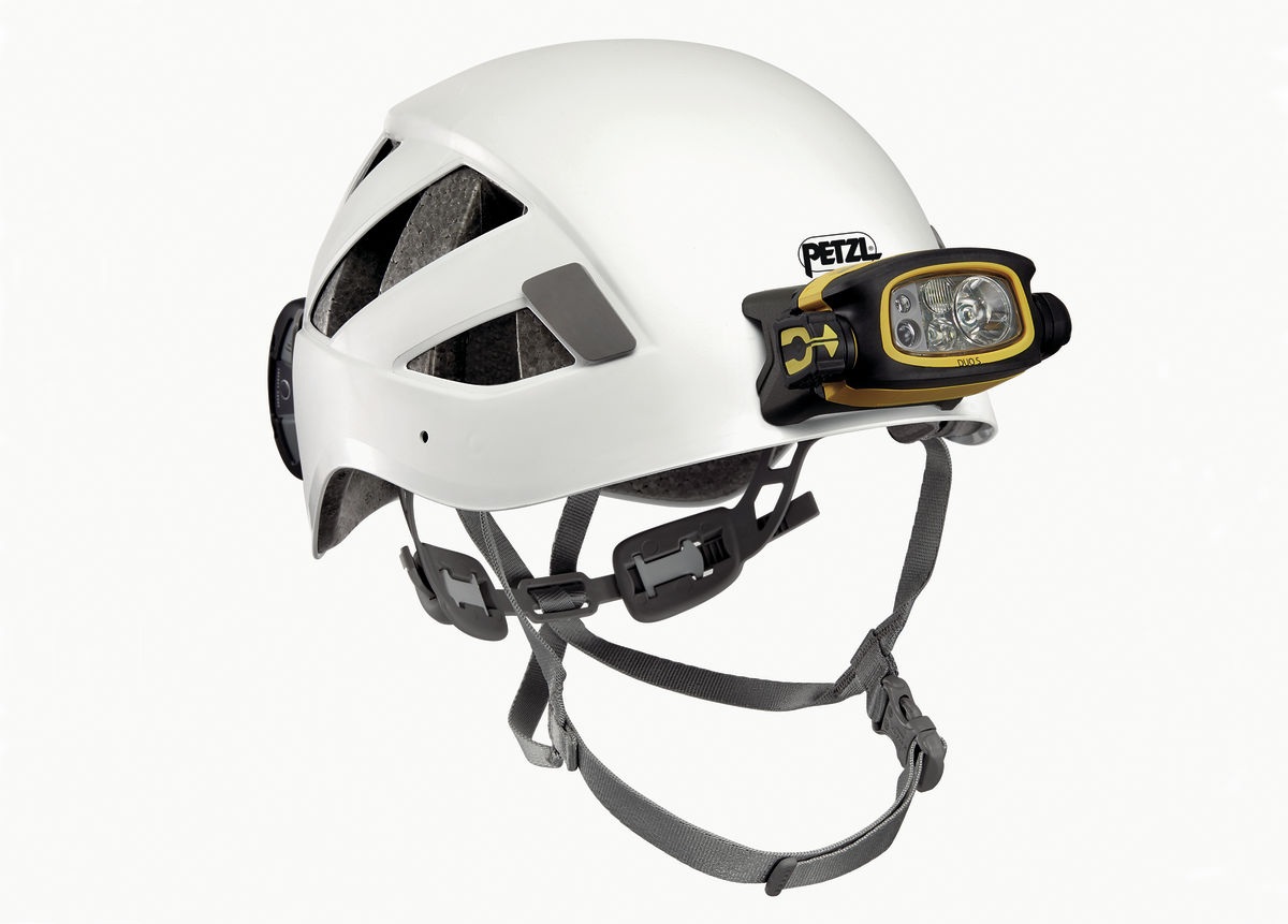 Čelovka Petzl DUO S nasadená na bielej prilbe Petzl — čierno-žlté svietidlo s optikami vpredu na držiaku, čierny akumulátor upevnený vzadu na škrupine, pod prilbou sivý podbradný popruh