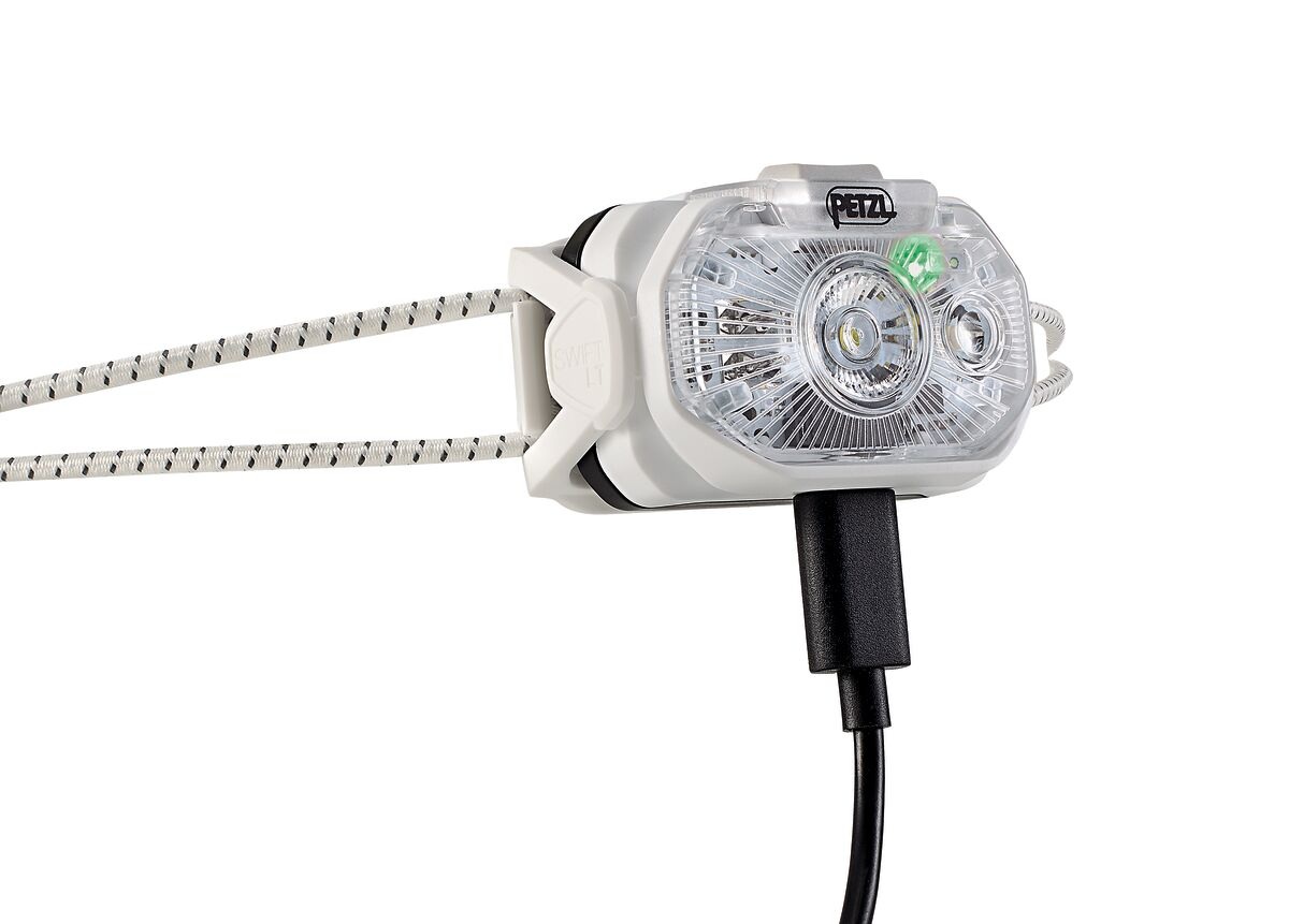 Petzl SWIFT LT pri nabíjaní — do spodnej strany tela je zapojený čierny kábel USB-C a v optike svieti zelený indikátor plného nabitia