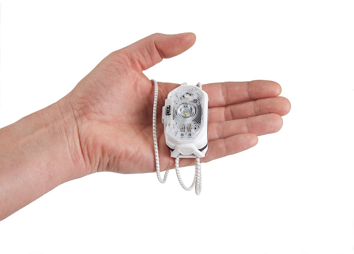 Petzl SWIFT LT položená v otvorenej dlani dospelého človeka, šnúry hlavového pásika voľne visia cez prsty — čelovka je menšia než dlaň