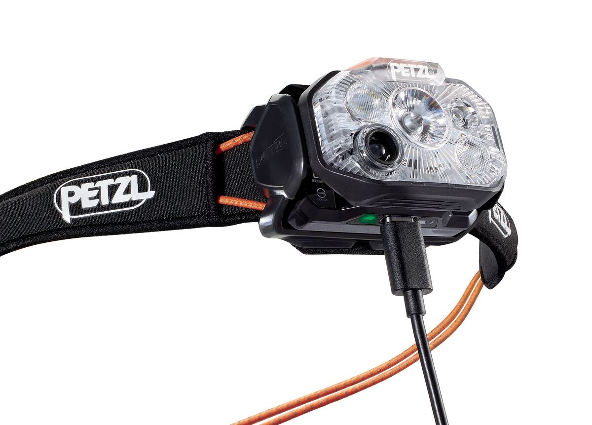 Petzl SWIFT RL pri nabíjaní — do akumulátora R2250 pod telom čelovky je zapojený kábel USB-C a svieti zelený indikátor plného nabitia