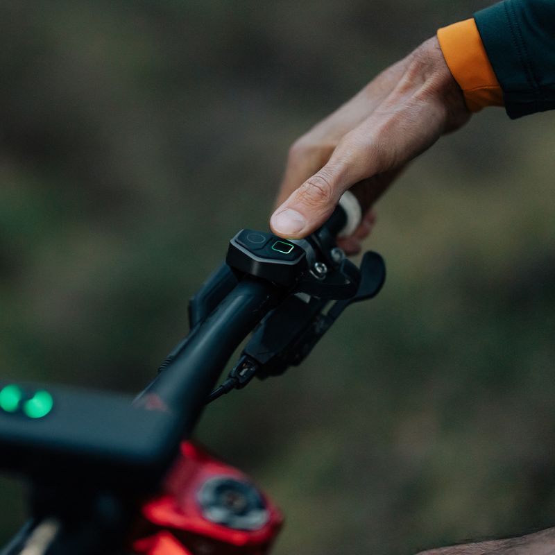 Palec na diaľkovom ovládači Magicshine MJ-6508 pripevnenom na riadidlách bicykla vedľa brzdovej páčky
