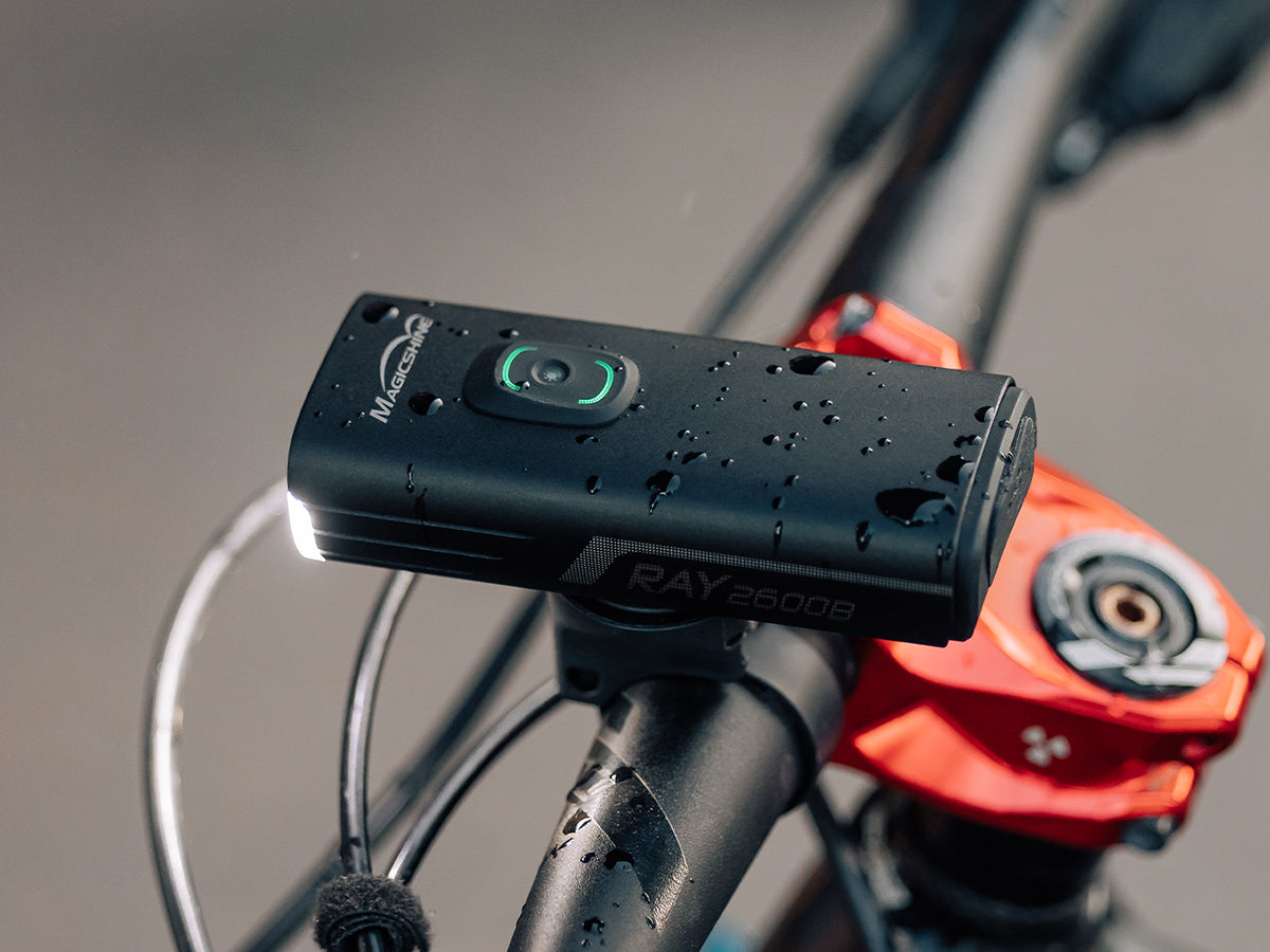 Magicshine RAY 2600B svieti na riadidlách bicykla pokrytý kvapkami vody — krytie IPX6 proti prúdiacej vode
