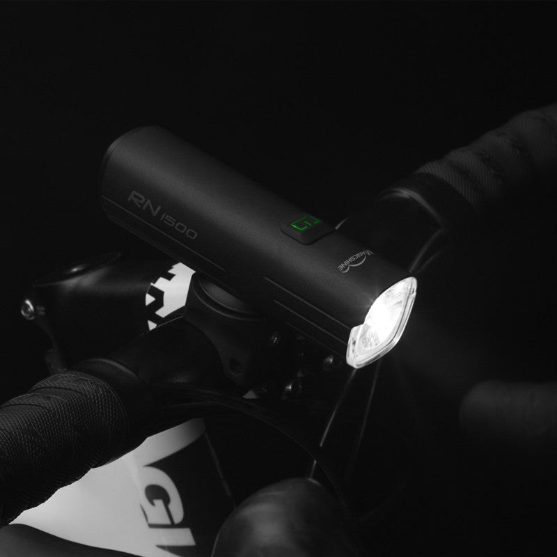 Magicshine RN1500 nasadený na riadidlách horského bicykla za tmy, na boku svieti zelená kontrolka batérie