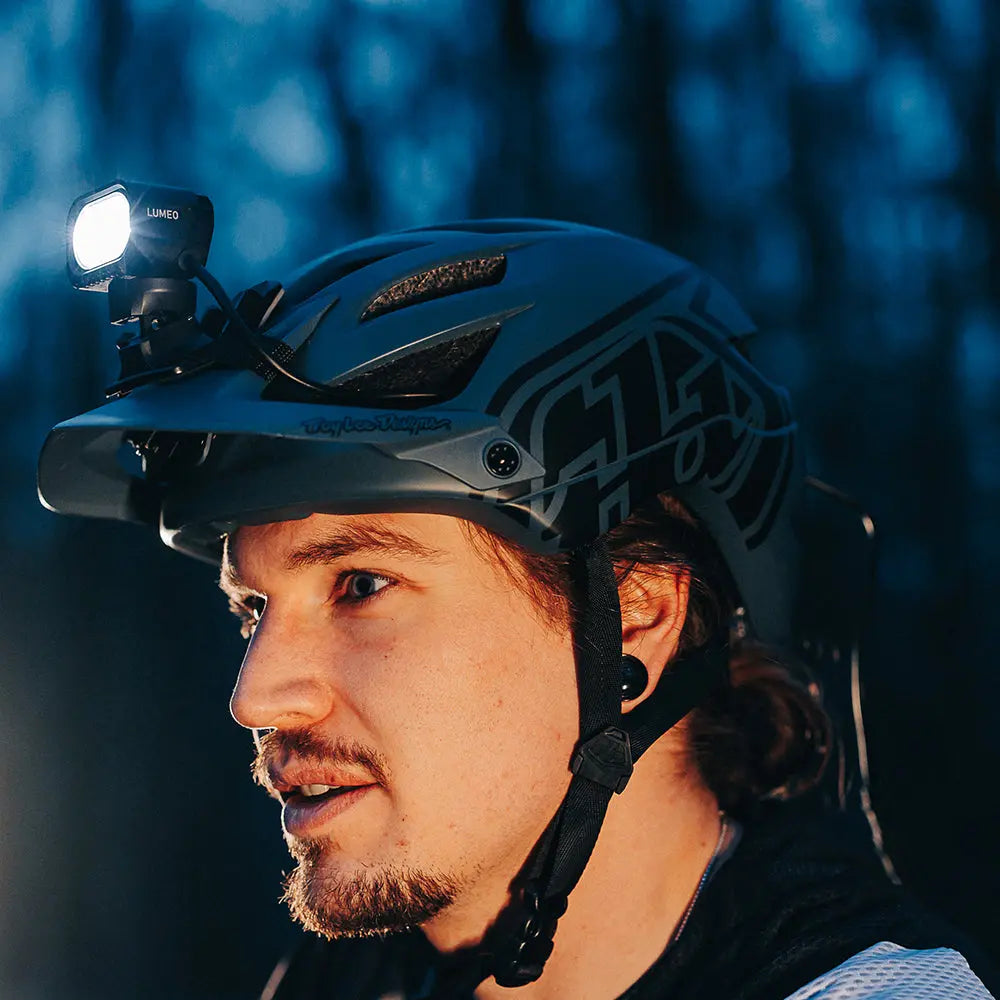 Rozsvietená Scoutlite LUMEO 4000 na držiaku na cyklistickej helme jazdca v nočnom lese