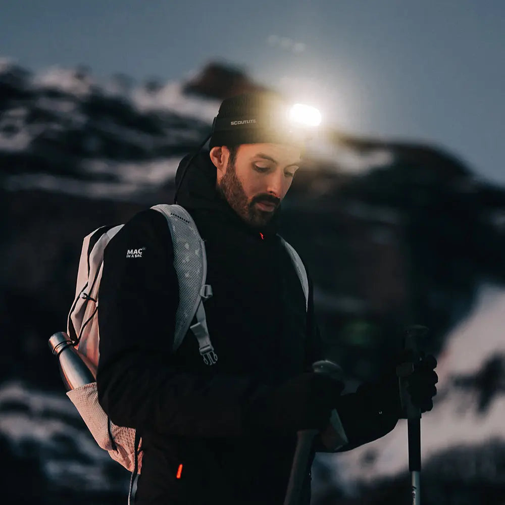 Skialpinista s rozsvietenou čelovkou Scoutlite MEGLE 6000 na nočnom výstupe s palicami a batohom