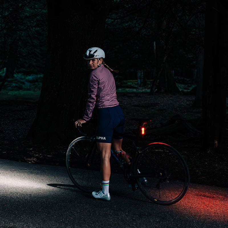 Fotografia výrobcu Magicshine: cyklistka v tmavom lese s rozsvieteným zadným svetlom SEEMEE 100AD a predným svetlom ovládaným cez FTR LightSync