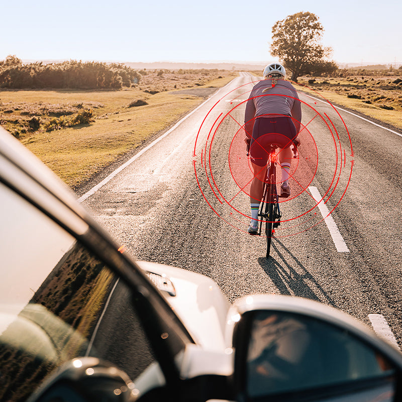Grafika výrobcu Magicshine: pohľad z auta na cyklistku so zadným svetlom SEEMEE 100AD, červené radarové kruhy znázorňujú detekciu blížiaceho sa vozidla