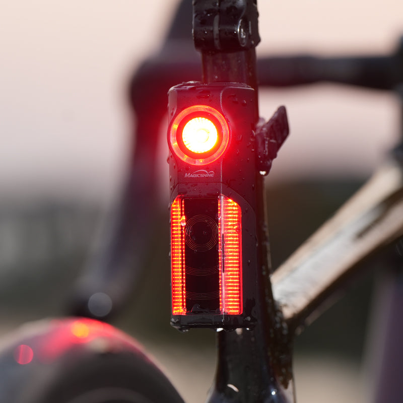 Fotografia výrobcu Magicshine: zadné svetlo SEEMEE R300 svieti na bicykli pokrytom kvapkami vody, krytie IPX6 proti dažďu