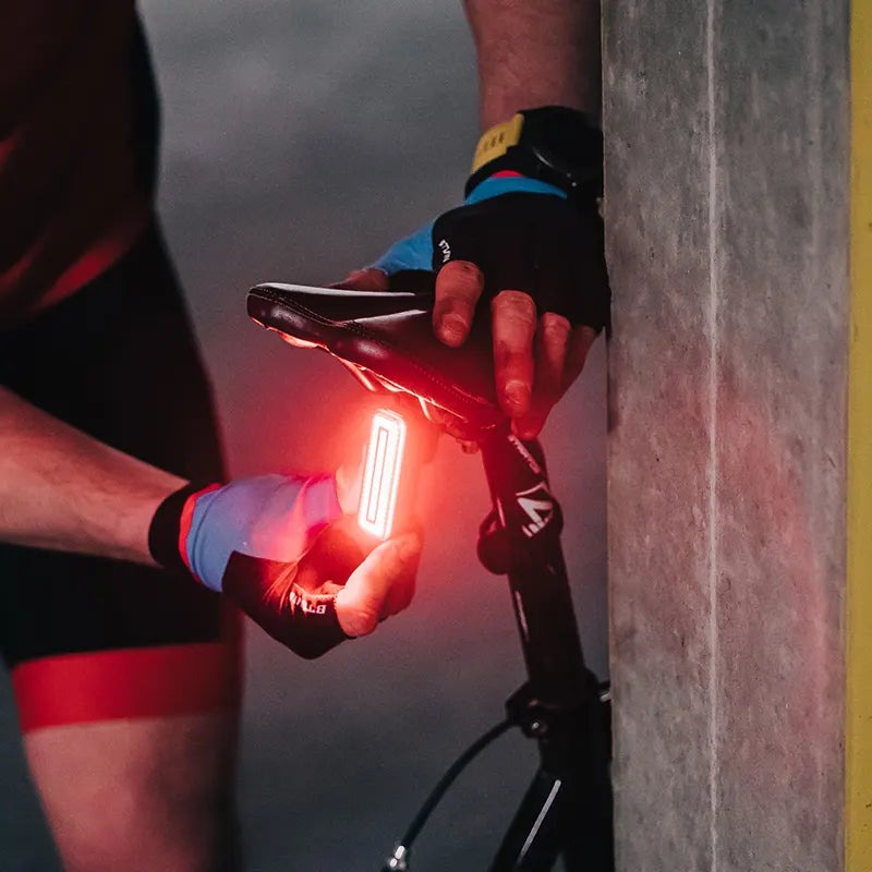 Cyklista drží rozsvietené zadné svetlo Magicshine SEEMEE 100 V2.0 pod sedlom bicykla za šera