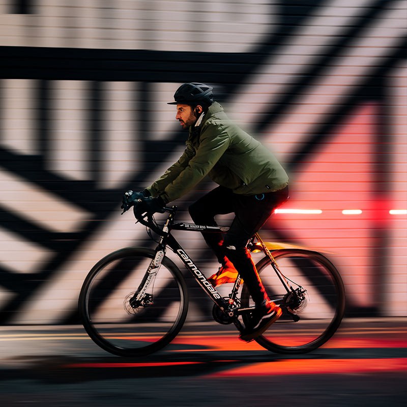 Cyklista v meste so zadným svetlom Magicshine SEEMEE 200 V3.0 pod sedlom, za ním červená stopa svetla na ceste