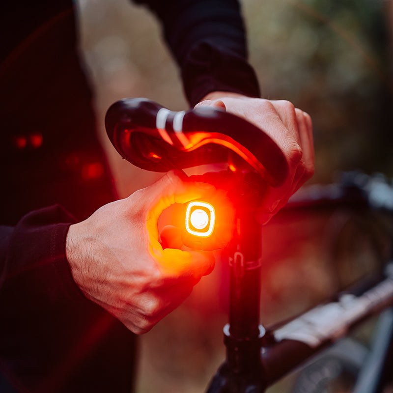 Ruka v rukavici stláča tlačidlo zadného svetla Magicshine SEEMEE 200 V3.0 upnutého pod sedlom bicykla