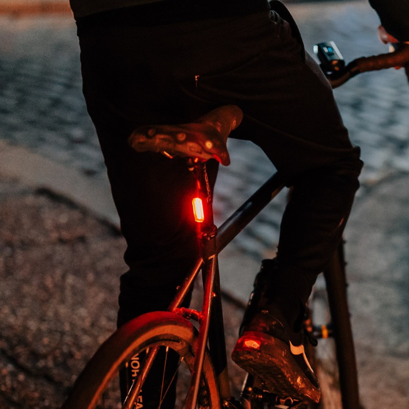 Cyklista na mestskej dlažbe za súmraku so zadným svetlom Magicshine SEEMEE 20 V2.0 na sedlovke