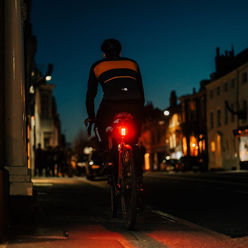 Cyklista v meste za šera so zadným svetlom Magicshine SEEMEE 300 pod sedlom, pohybový senzor reaguje na spomalenie