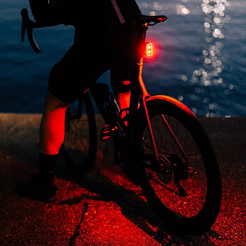 Bicykel spredu v noci, zadné svetlo Magicshine SEEMEE 300 osvetľuje asfalt červeným svetlom okolo celého kolesa