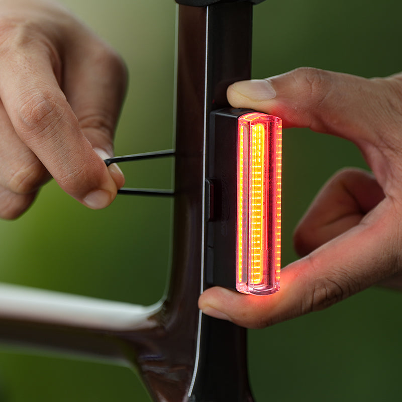 Ruky nasadzujú rozsvietené zadné svetlo Magicshine SEEMEE 50 V2.0 silikónovým remienkom na sedlovku bicykla