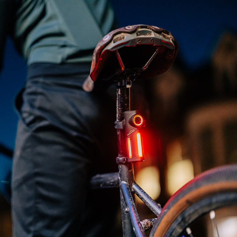 Cyklista jazdí v noci mestom, zadné svetlo Magicshine SEEMEE DV s kamerou svieti načerveno pod sedlom