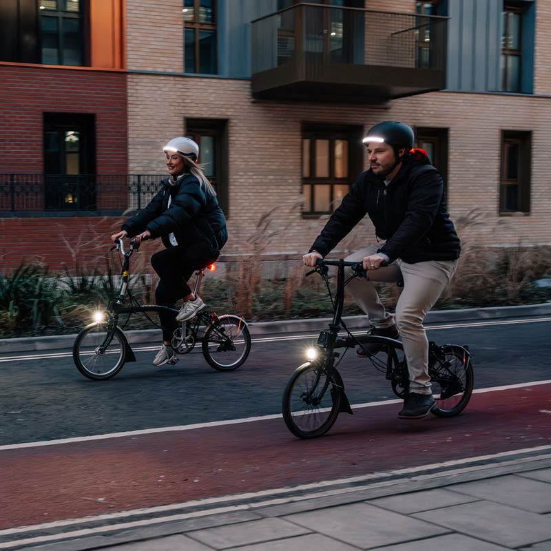 Dvaja cyklisti na skladacích bicykloch Brompton v meste za šera, vpredu im svieti Magicshine VTG 1000