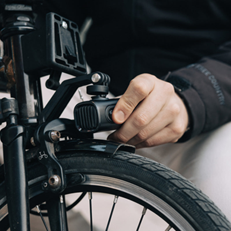 Ruka nasadzuje svetlo Magicshine VTG 1000 na vidlicový držiak priskrutkovaný k prednej brzde skladacieho bicykla Brompton