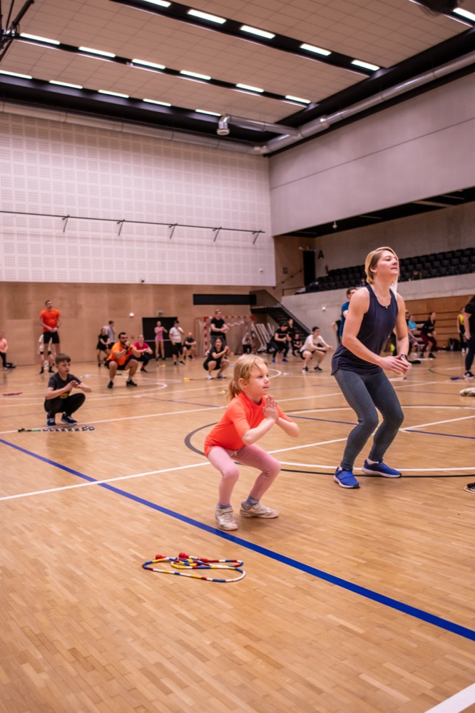Mamka skáče přes švihadlo vedle malé dcery ve sportovní hale