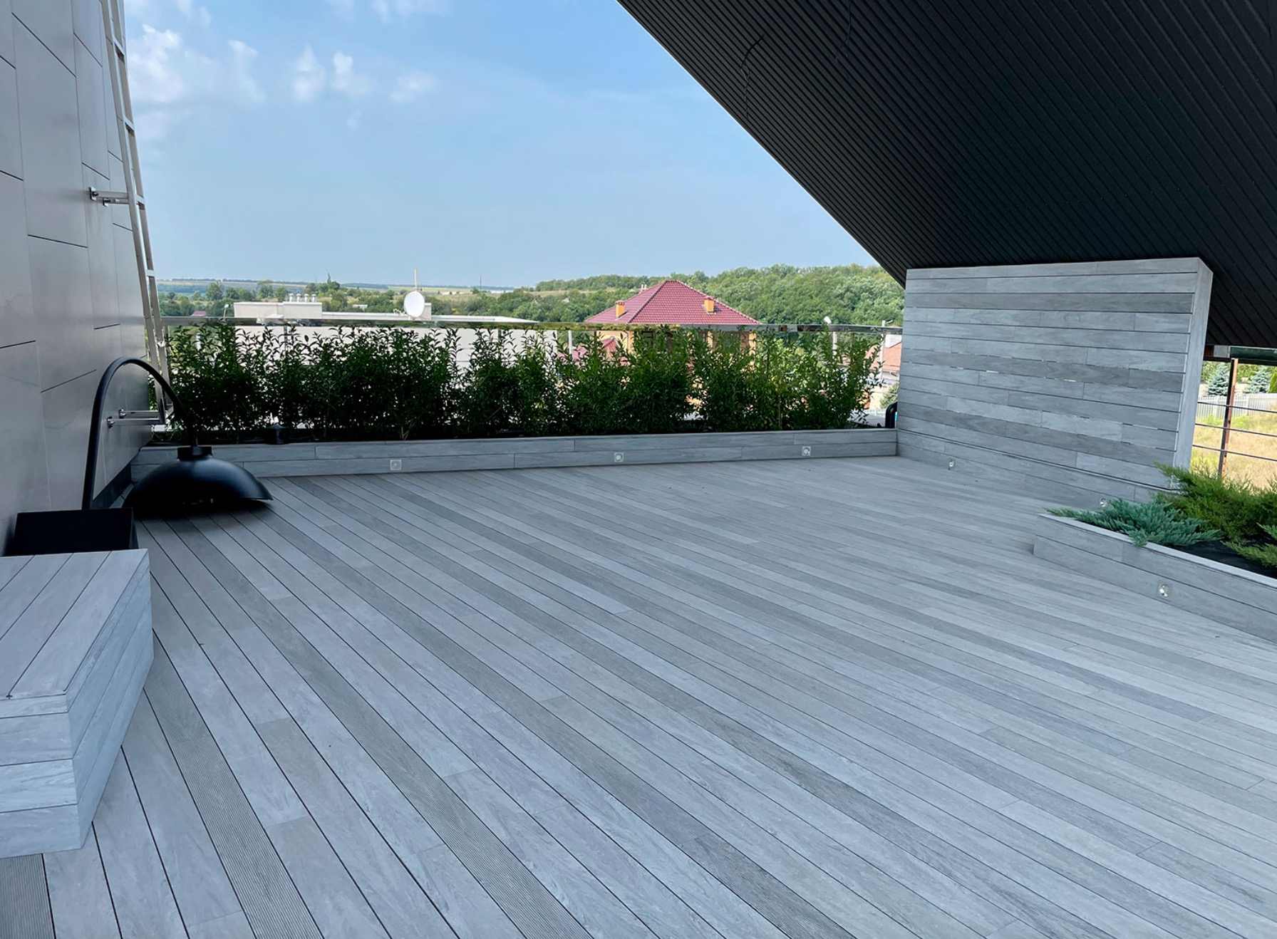 svetla-wpc-terasa-na-strese-so-zelenymi-krikmi-po-okraji-a-vyhladom-na-strechy-okolitych-domov
