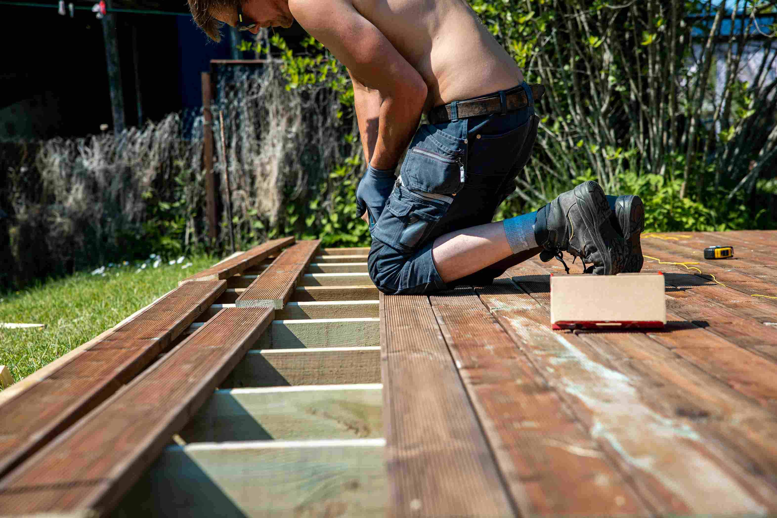 muz-v-pracovnych-nohaviciach-a-pracovnych-rukaviciach-vymiena-po-zime-poskodene-a-nevzhladne-terasové-wpc-dosky-na-drevenej-terasovej-konstrukcii