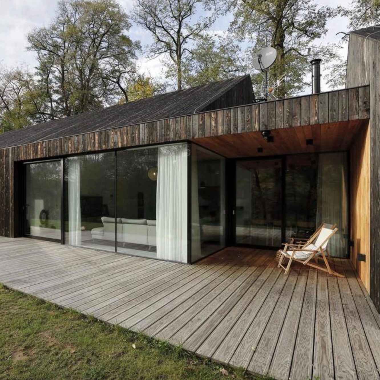 tmava-modernisticka-chata-s-presklenou-stenou-a-wpc-terasou-v-sivom-odtieni-v-lesnom-prostredi-ticha-lesna-architektura