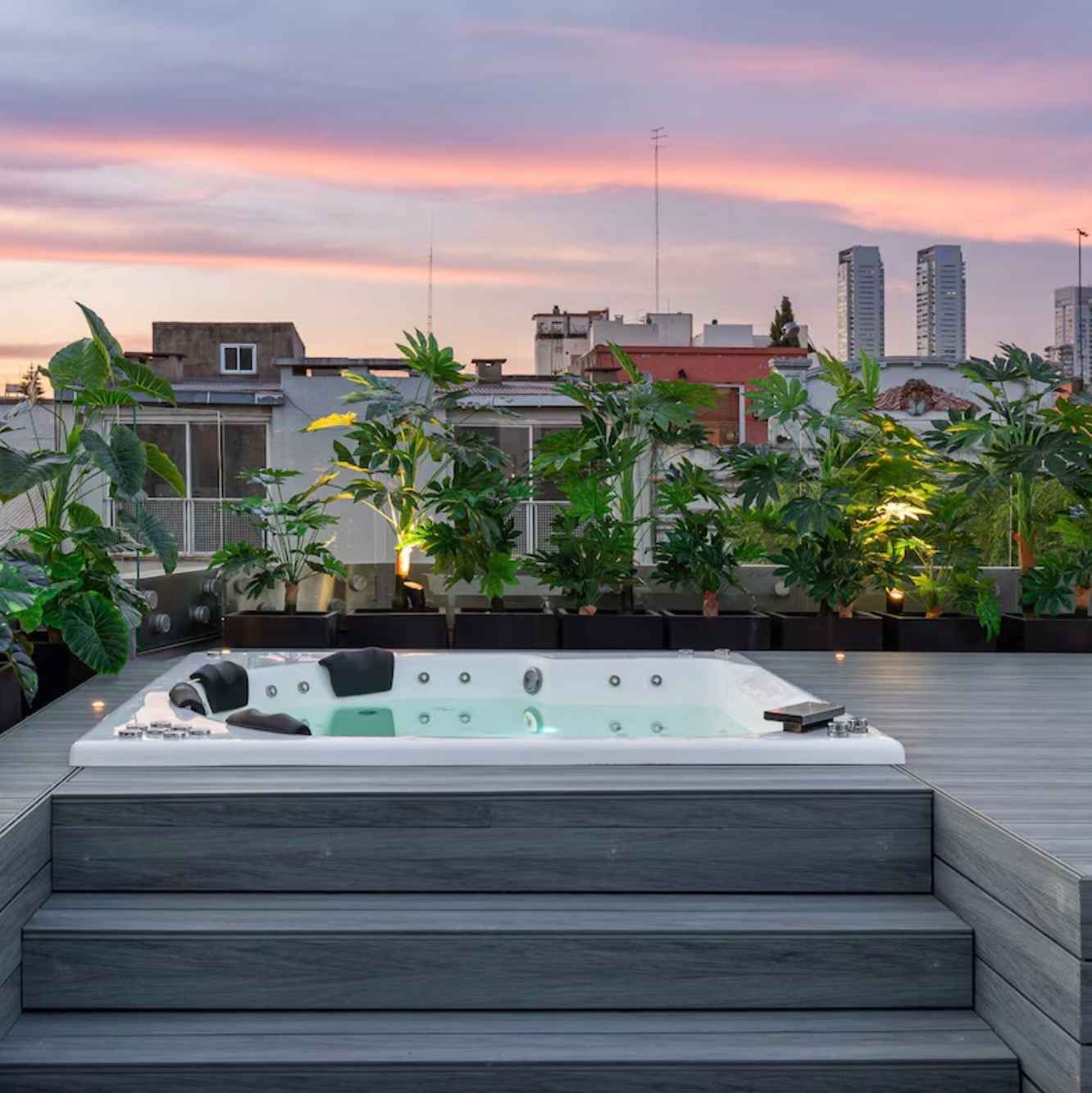 stresna-terasa-s-vstavanou-bielou-virivkou-oblozenou-sivymi-wpc-doskami-velkymi-kvetinacmi-s-tropickymi-rastlinami-a-zapadom-slnka-v-pozadi-mestska-oaza-pokoja