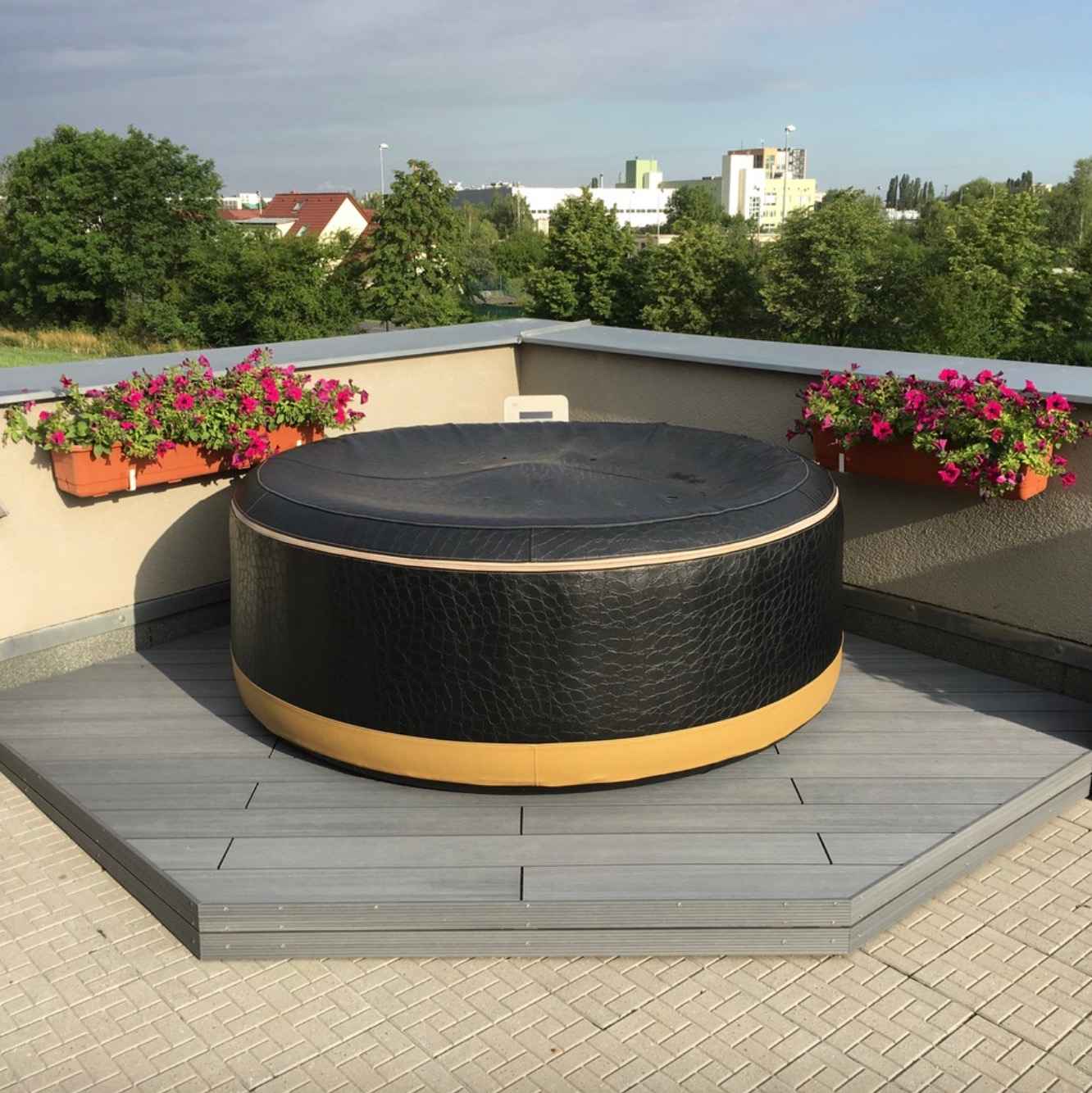 nafukovacia-virivka-na-terase-sivych-wpc-dosiek-obklopena-betonovou-dlazbou-a-kvetinacmi-s-ruzovymi-kvetmi-jemny-kontrast-materialov-a-prirody