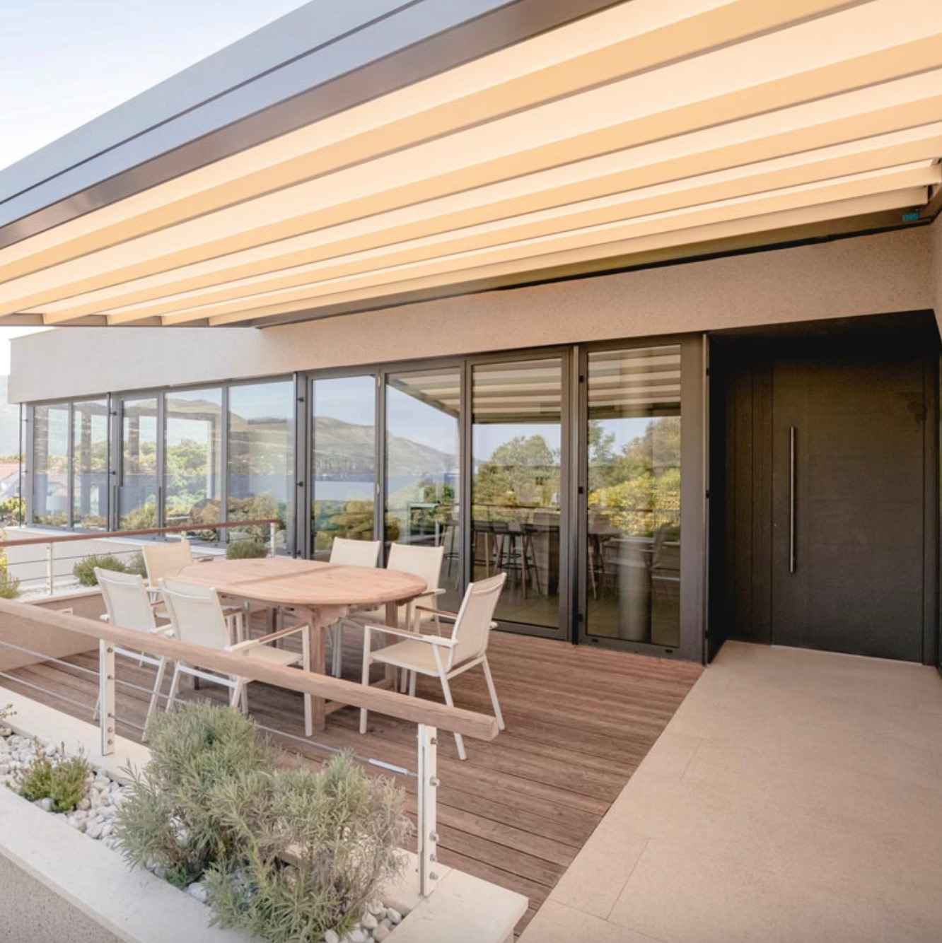 priestranna-terasa-s-kombinaciou-svetlej-dlazby-a-prirodzene-hnedej-wpc-podlahy-s-velkym-okruglym-stolom-bielymi-stolickami-a-vyhladom-na-prirodu-vkusne-a-harmonicke