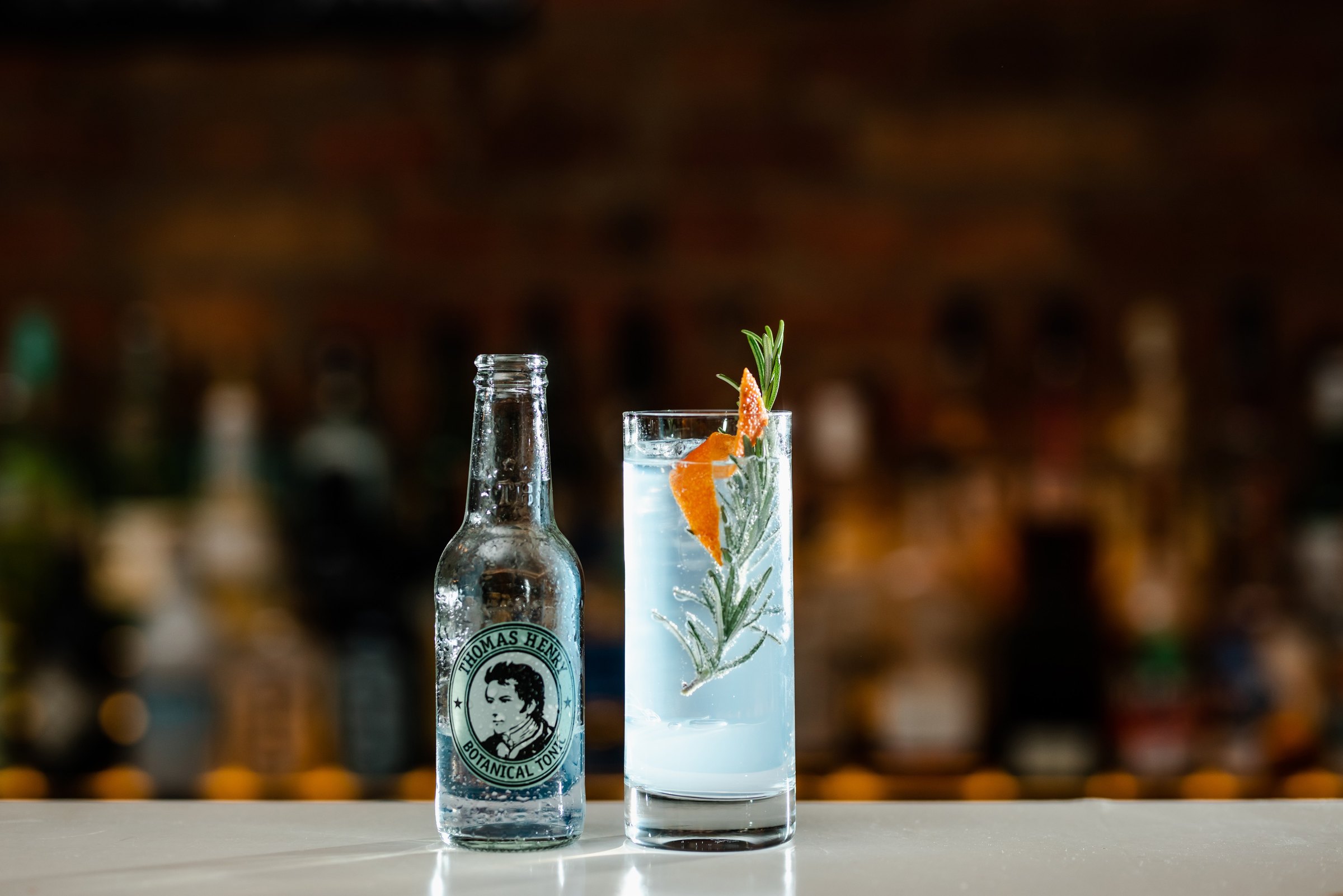 Botanical gin tonic s rozmarýnem a láhev Thomas Henry Botanical Tonic na baru