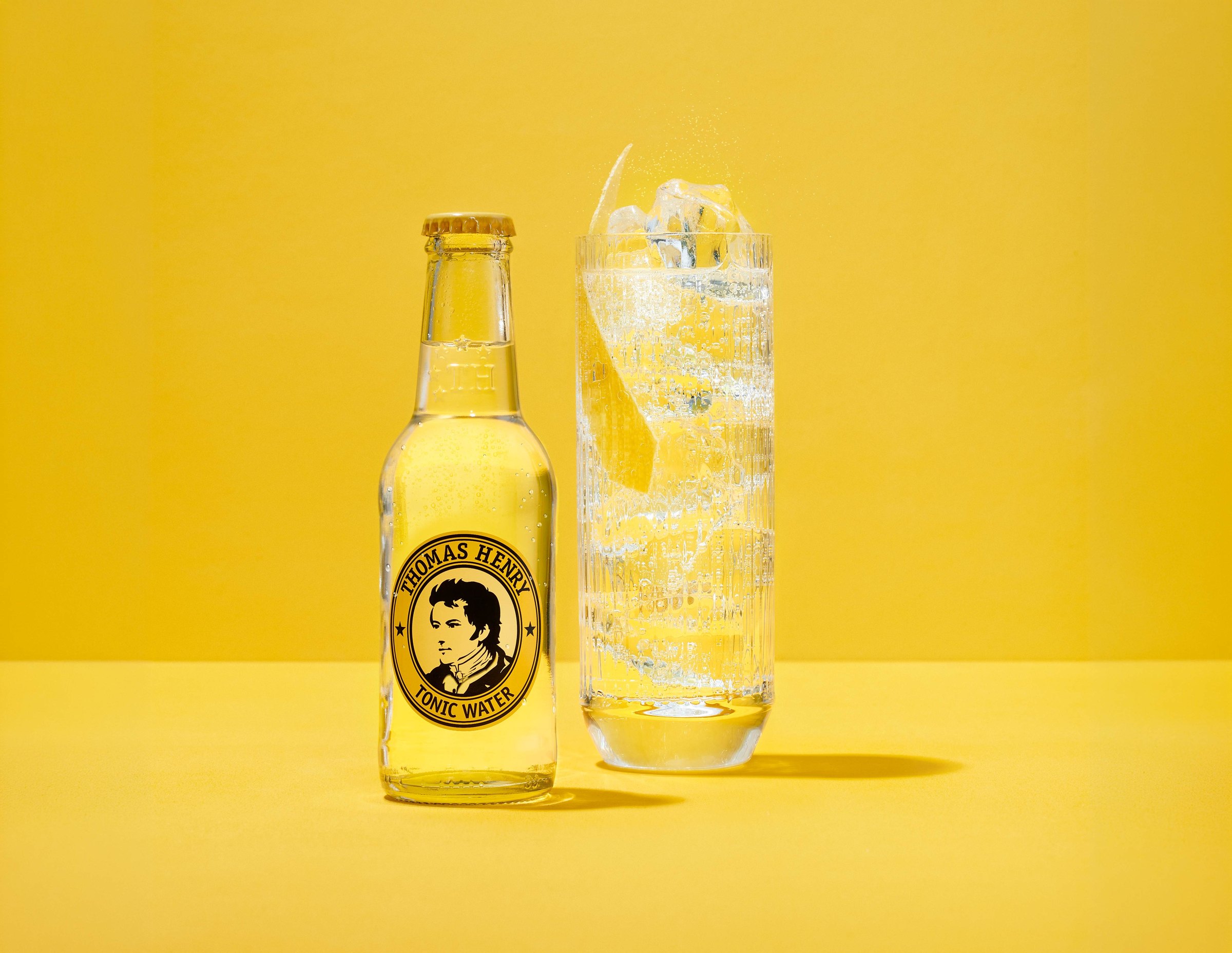 Láhev Thomas Henry Tonic Water a sklenice s ledem a citronem na žlutém pozadí