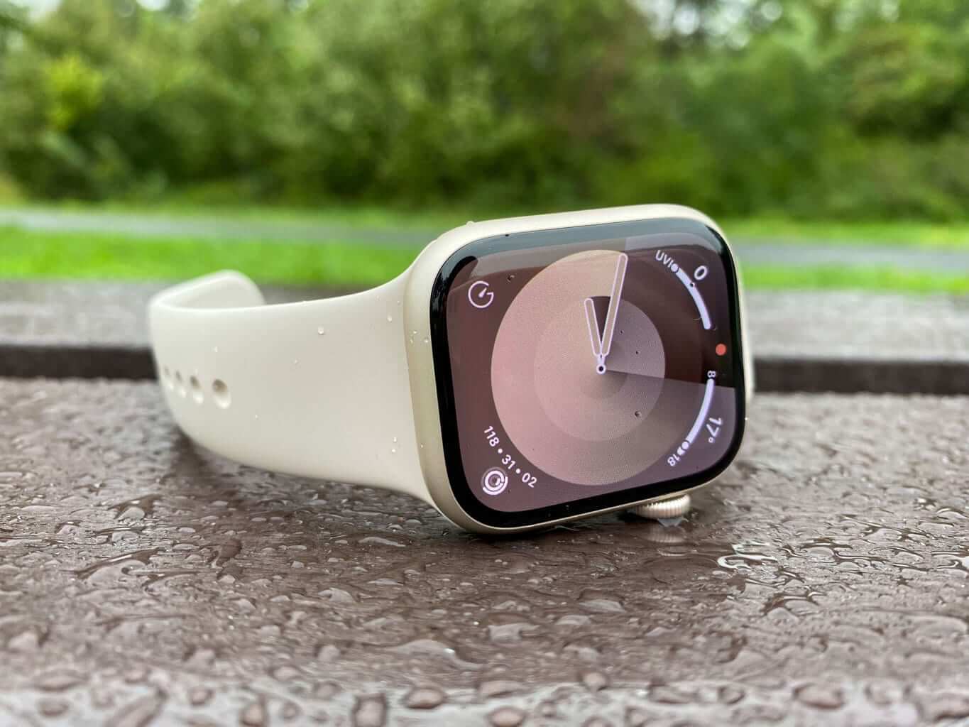 Biele watch series 9 vyfotené z boku na mokrej lavičke. 