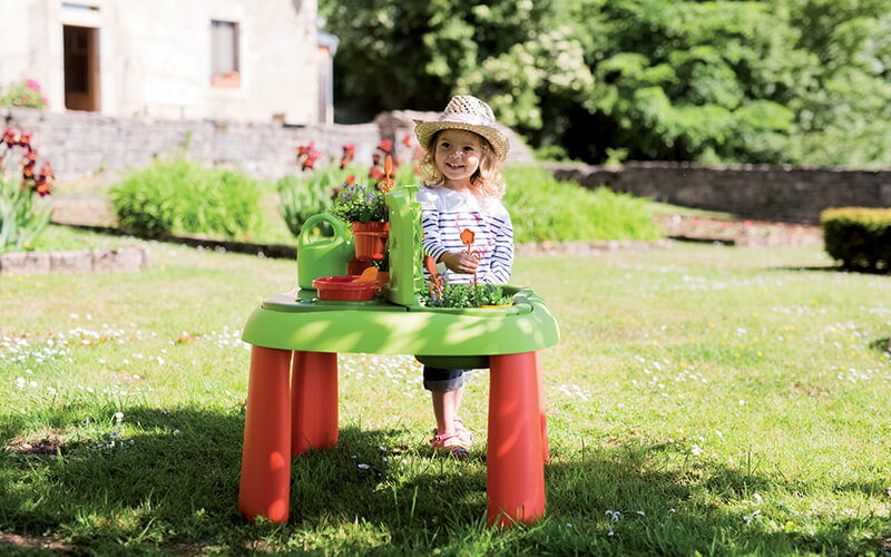Malé dievčatko stojace na záhrade pred stolíkom. 