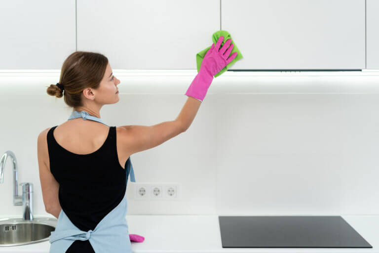 Žena čistiaca kuchynské horné skrinky. 